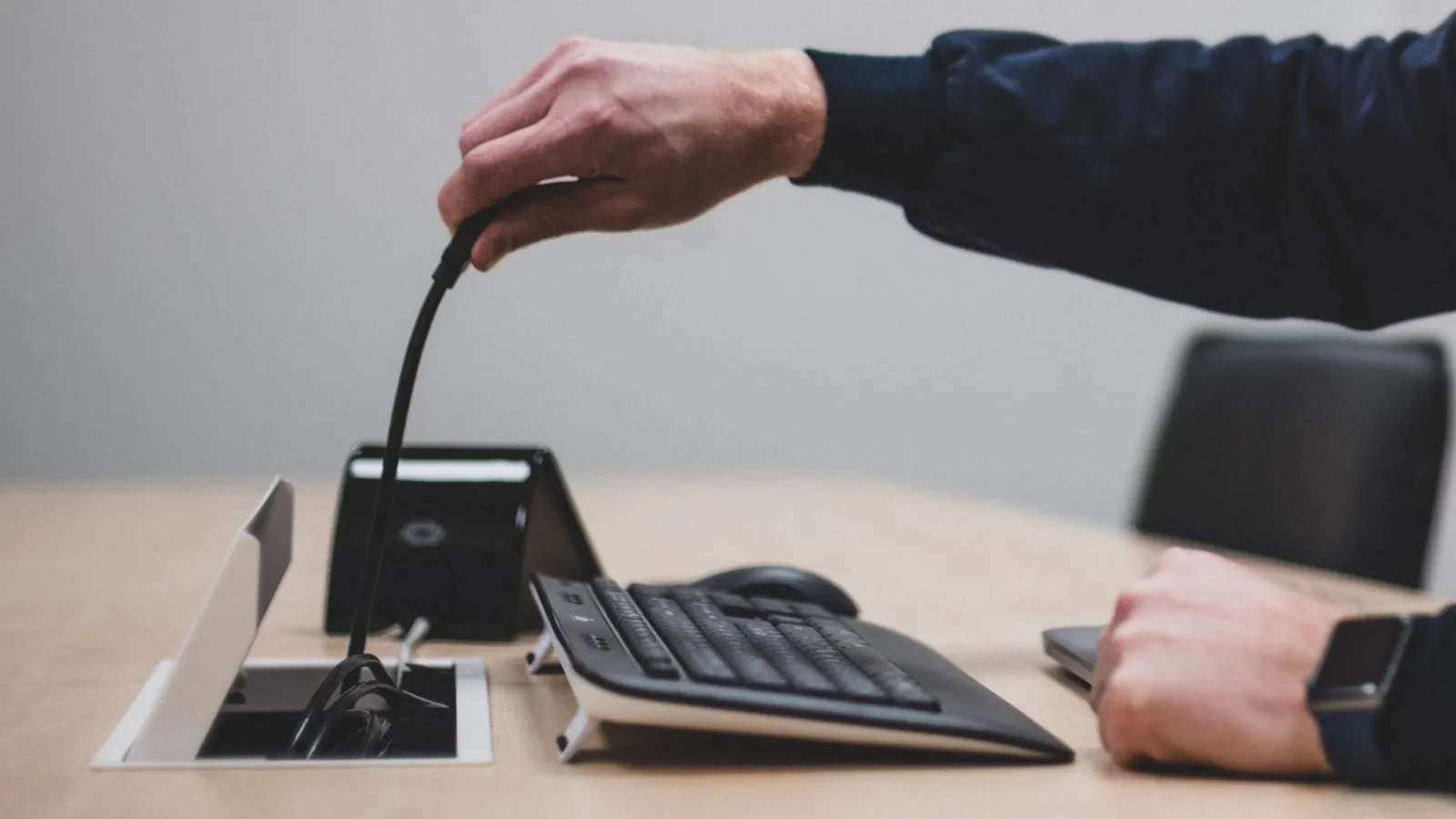 Hand som drar upp en HDMI-kabel ur bordsbrunnen.