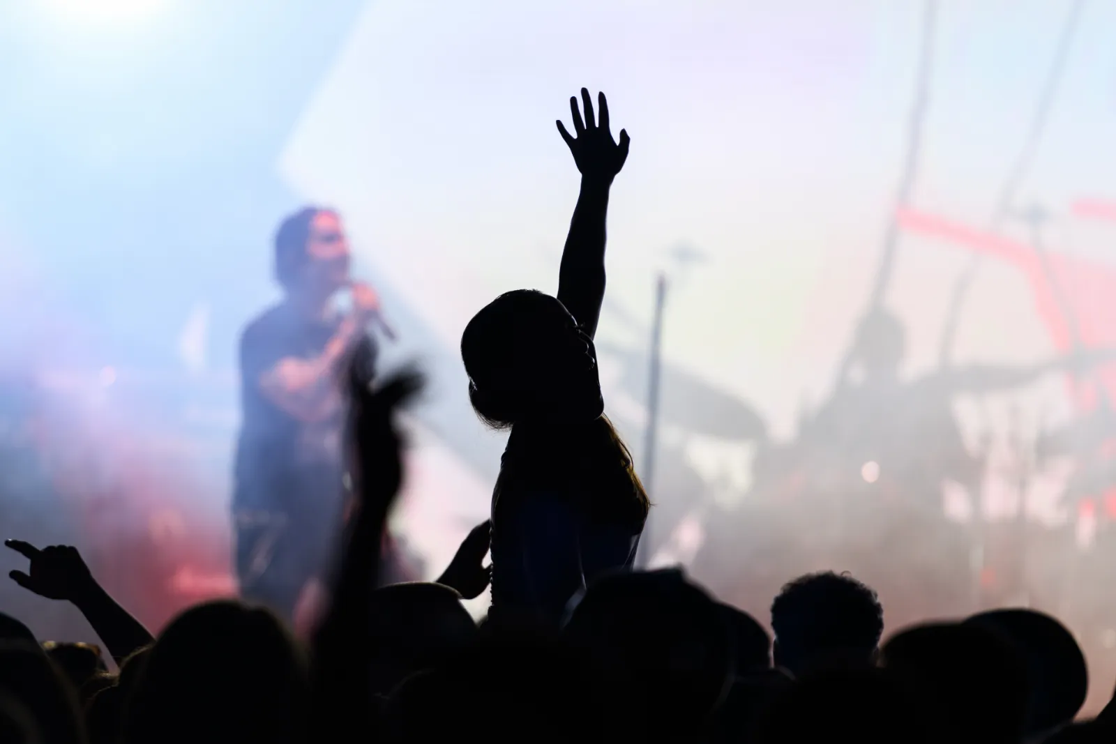 Konsertpublik med uppsträckt hand framför artist på upplyst scen