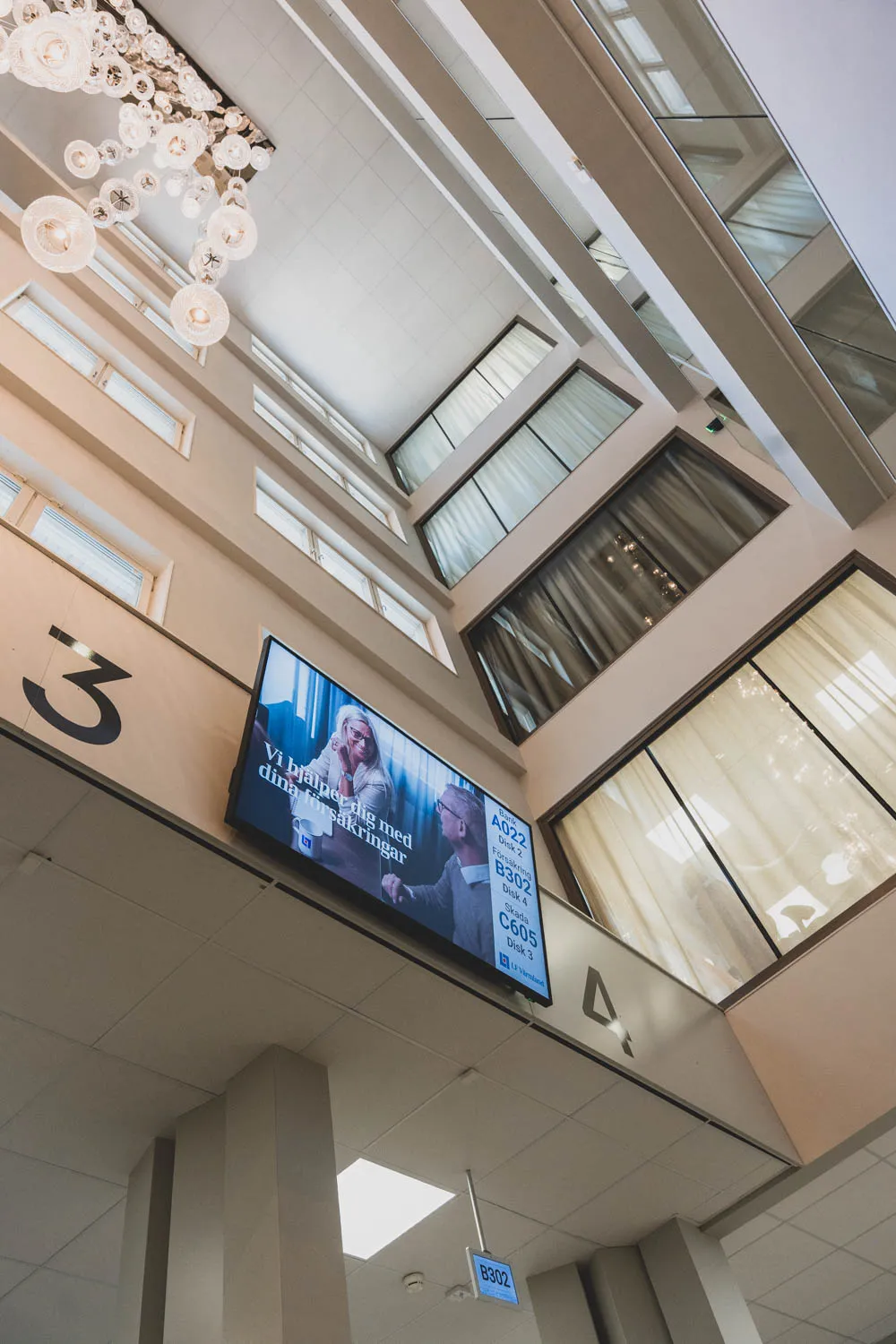 Digital skyltning i Länsförsäkringar Värmlands reception – kösystem med disknummer på storbildsskärm under det höga atriumtaket.